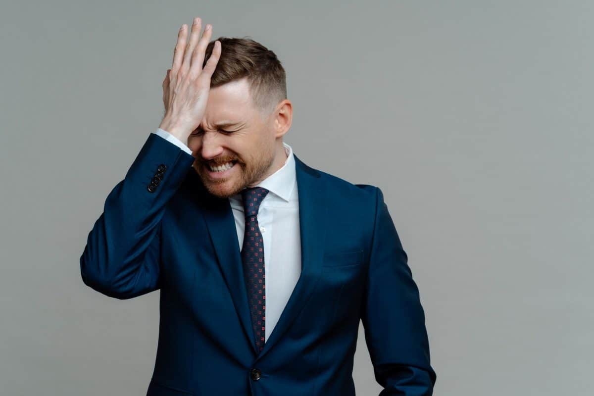 man with his hand on his forehead while gritting his teeth. Look of regret.