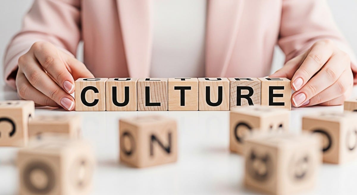 Woman arranging wooden blocks spelling CULTURE on a white table