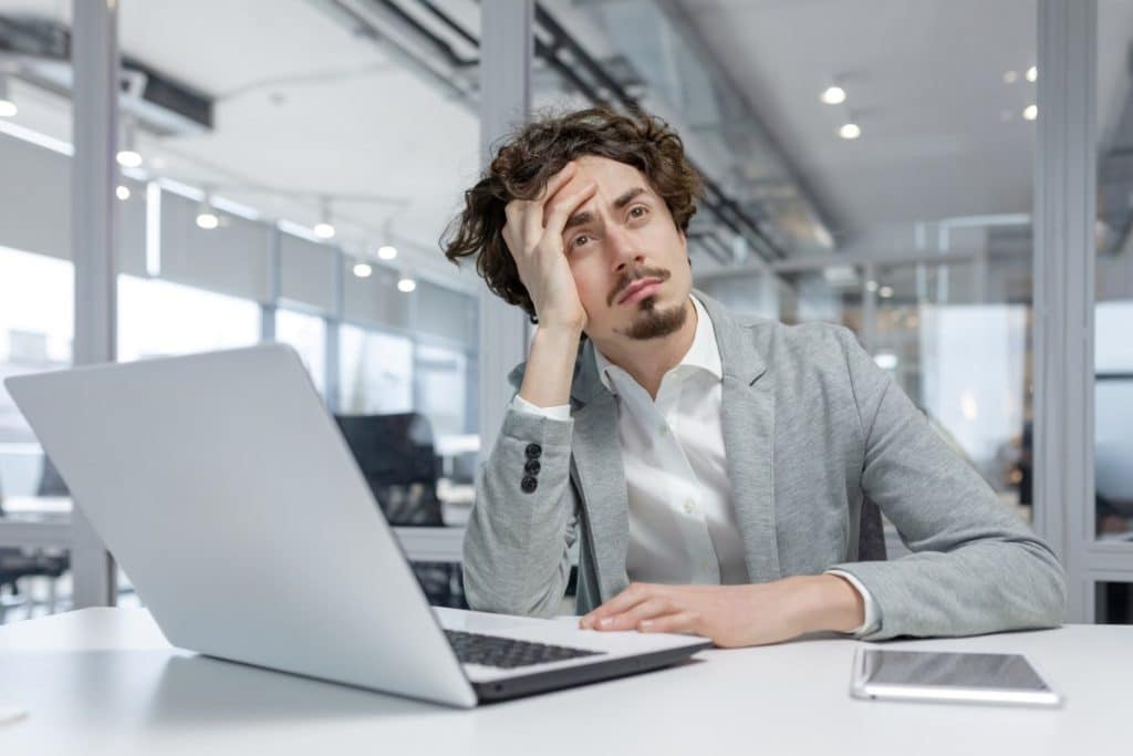 Stressed young businessman with curly hair pondering solutions at his desk