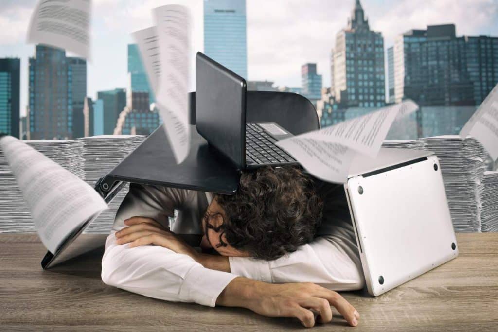 Tired businessman sleeping under a pile of laptops due to workload