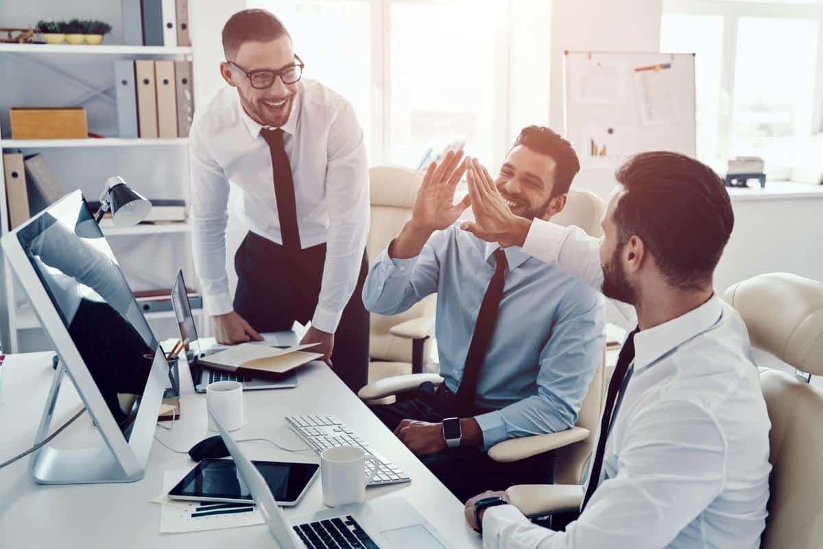 High five for success. Group of young modern men in formalwear smiling while working in the office
