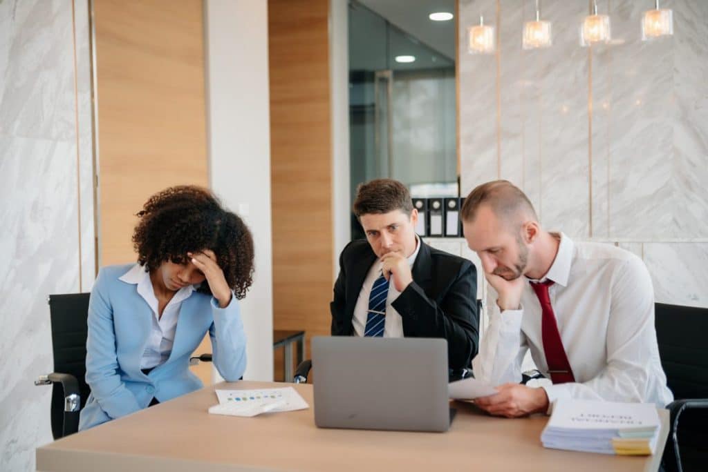 Team thinking of problem solution at office meeting, sad diverse business people group shocked by bad news